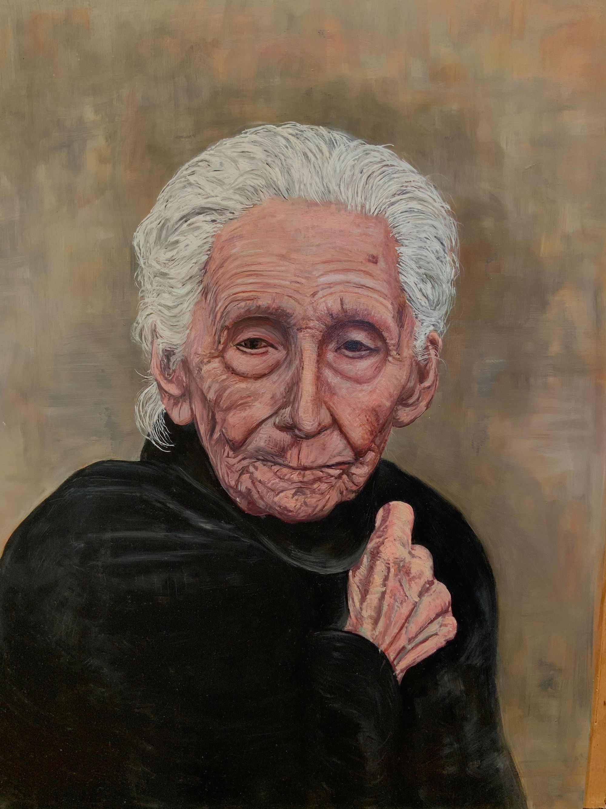 An old woman with weathered face looks slightly down while clutching her hand to her shoulder holding a shawl around her.