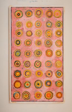 An abstract painting of concentric circles of yellow, orange and red arranged in a 5 x 9 grid hangs on a wall.